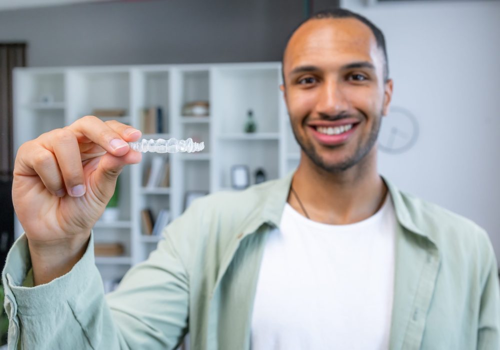 Young handsome man holding aligner standing with a happy face and smiling showing teeth