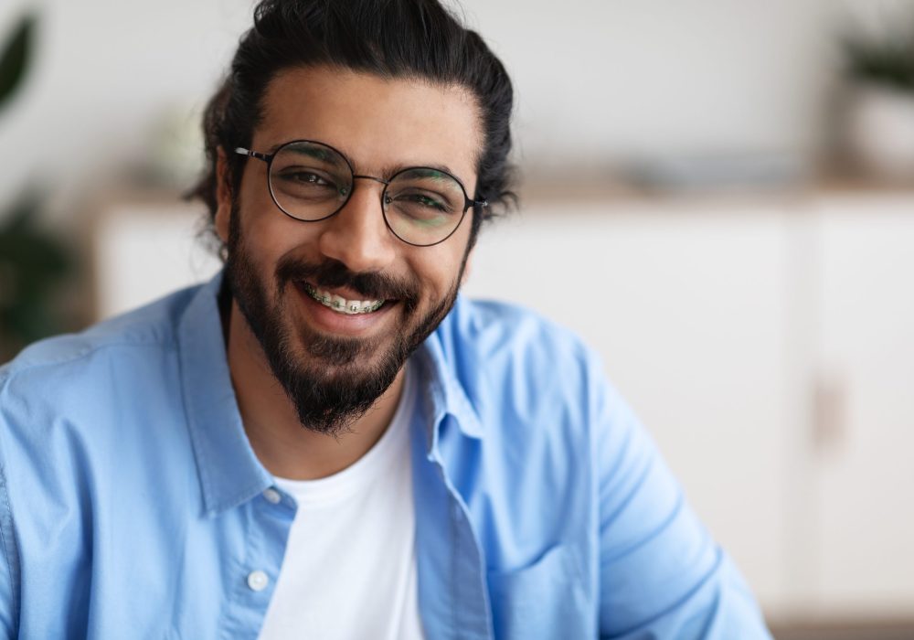 Closeup Portrait Of Positive Arab Guy With Dental Braces And Eyeglasses Smiling At Camera, Handsome Bearded Millennial Man With Brackets On Teeth Posing Indoors, Selective Focus With Copy Space